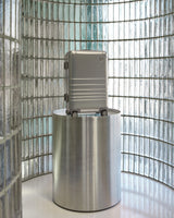 Silver suitcase on a metallic stand against a glass brick wall.