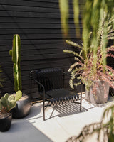 Black metal bench with potted plants against a black wooden wall