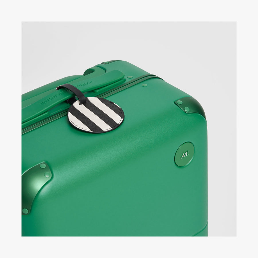 Jungle Green | Close-up view of the logo detail on a Hybrid suitcase in Jungle Green, paired with a Poplin Stripe Black luggage tag