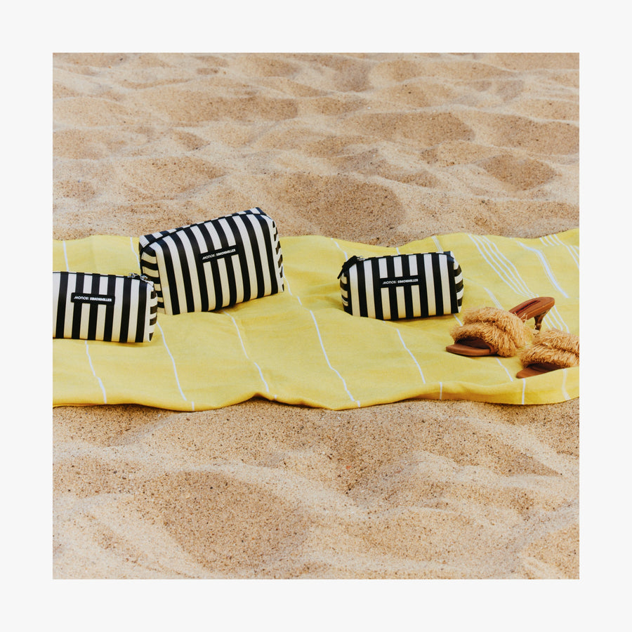 Large / Poplin Stripe Black | Three Metro Toiletry Cases in Poplin Stripe Black arranged on a yellow towel laid out on sandy beach