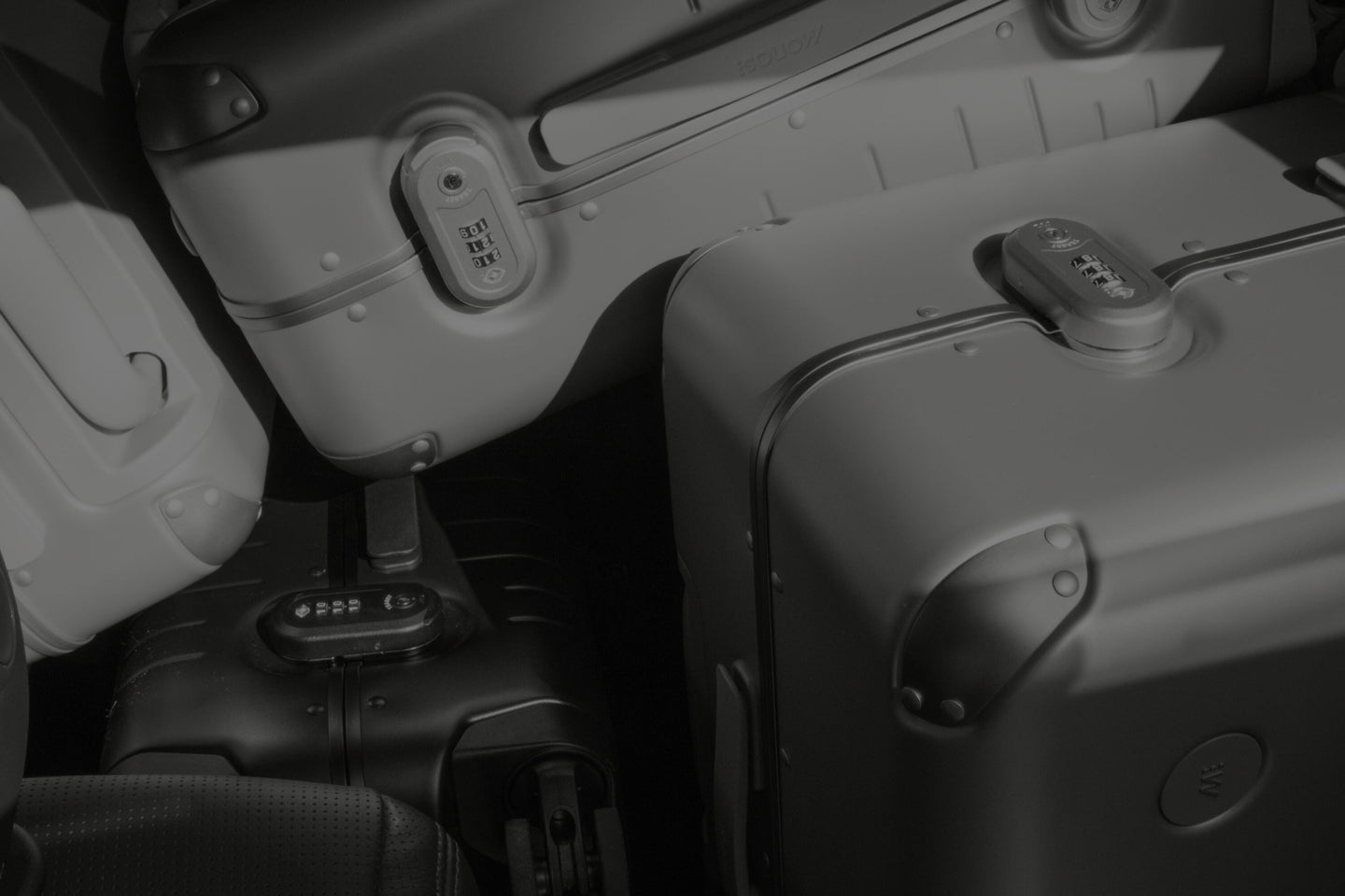 A close-up of stacked Hybrid suitcases in a monochromatic lighting setting. The suitcases feature built-in TSA-accepted locks and smooth surfaces, emphasizing their durable and sleek design. Whisper-quiet spinner wheels are partially visible, suggesting the luggage is optimized for mobility.