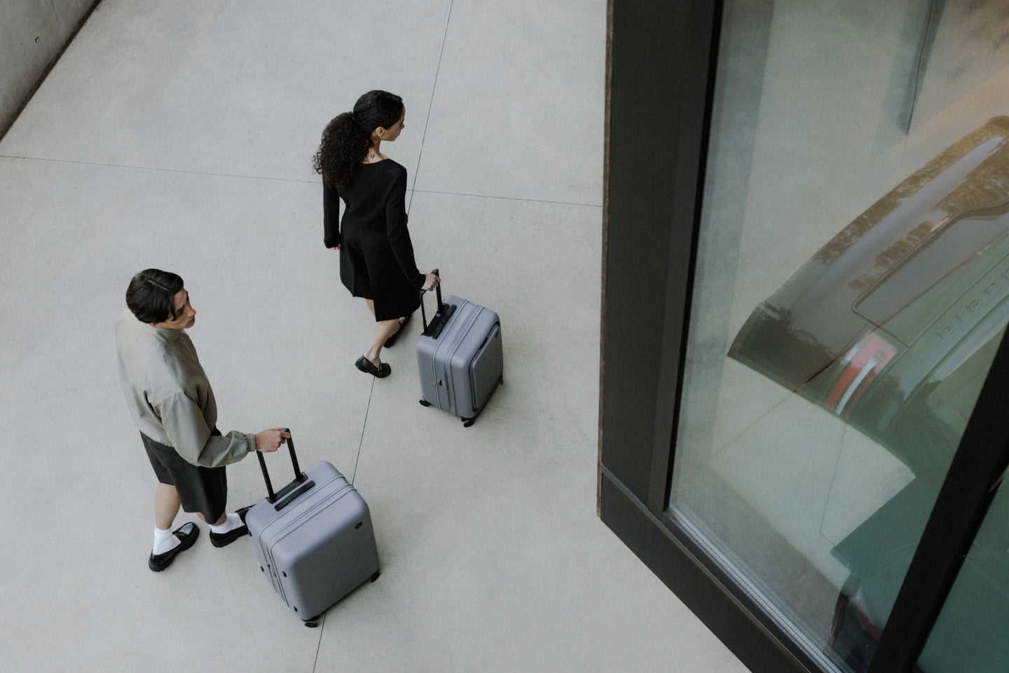 A man and a woman walk across a concrete surface, each pulling an Expandable luggage in Storm Grey.