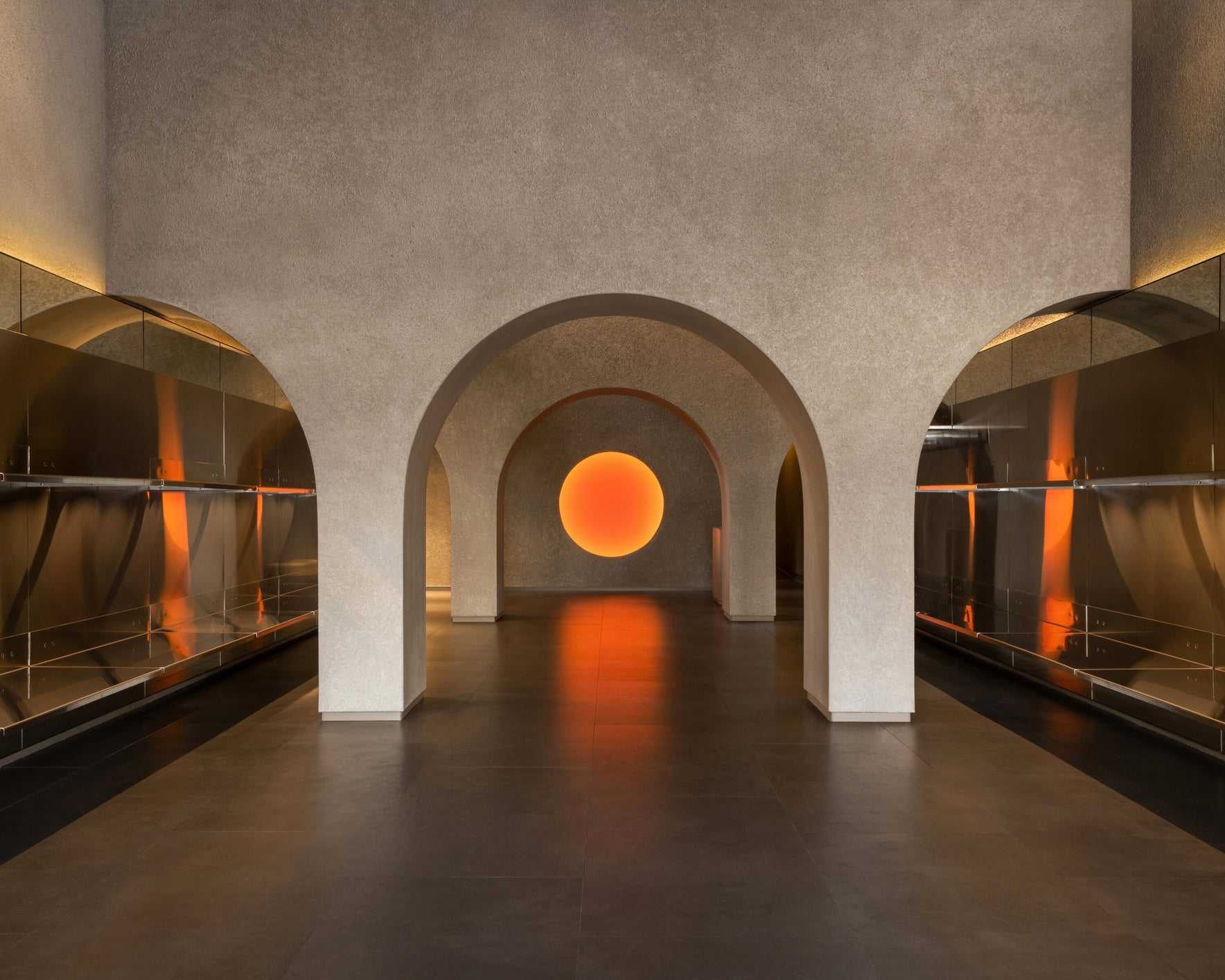 Monos Georgetown store interior in Washington, D.C., with arched architecture, stainless steel shelving, and a glowing circular light centerpiece.