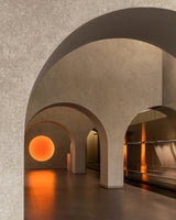 Arched passageways inside the Monos Georgetown store, illuminated by a warm circular light reflecting across textured stone and mirrored surfaces.