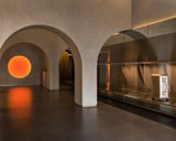 Arched interior of the Monos Georgetown store, featuring a glowing circular light installation and brushed steel shelving displaying aluminum luggage.
