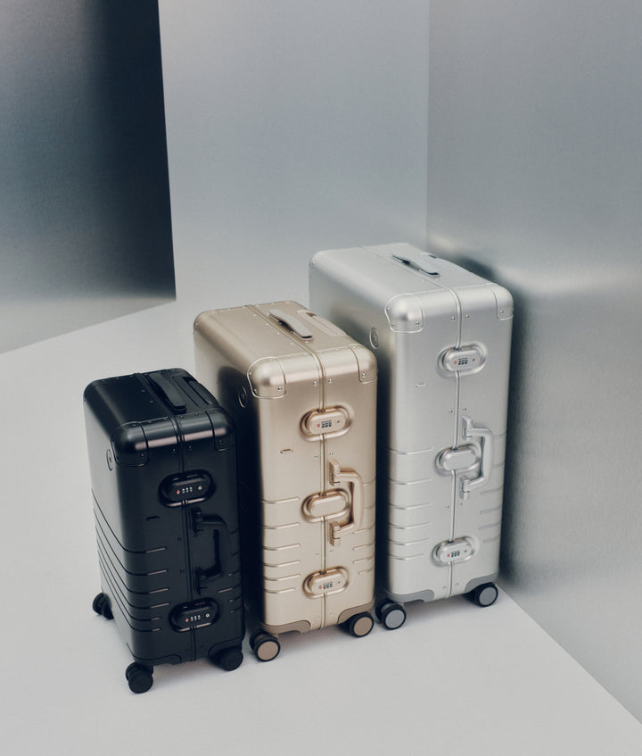 The Monos Aluminum Collection featuring the Carry-On in Caviar Black, Check-In Medium in Champagne Gold, and Check-In Large in Aspen Silver. The sleek aluminum shells and minimalist design highlight Monos’ signature craftsmanship and timeless travel aesthetic.
