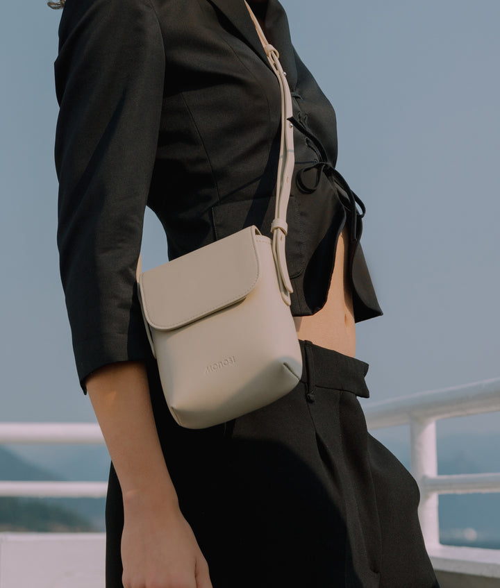 The Monos Metro Mini Crossbody in Ivory, worn across the body with a sleek black outfit against a bright sky. A compact, minimalist bag designed for hands-free ease and everyday elegance.