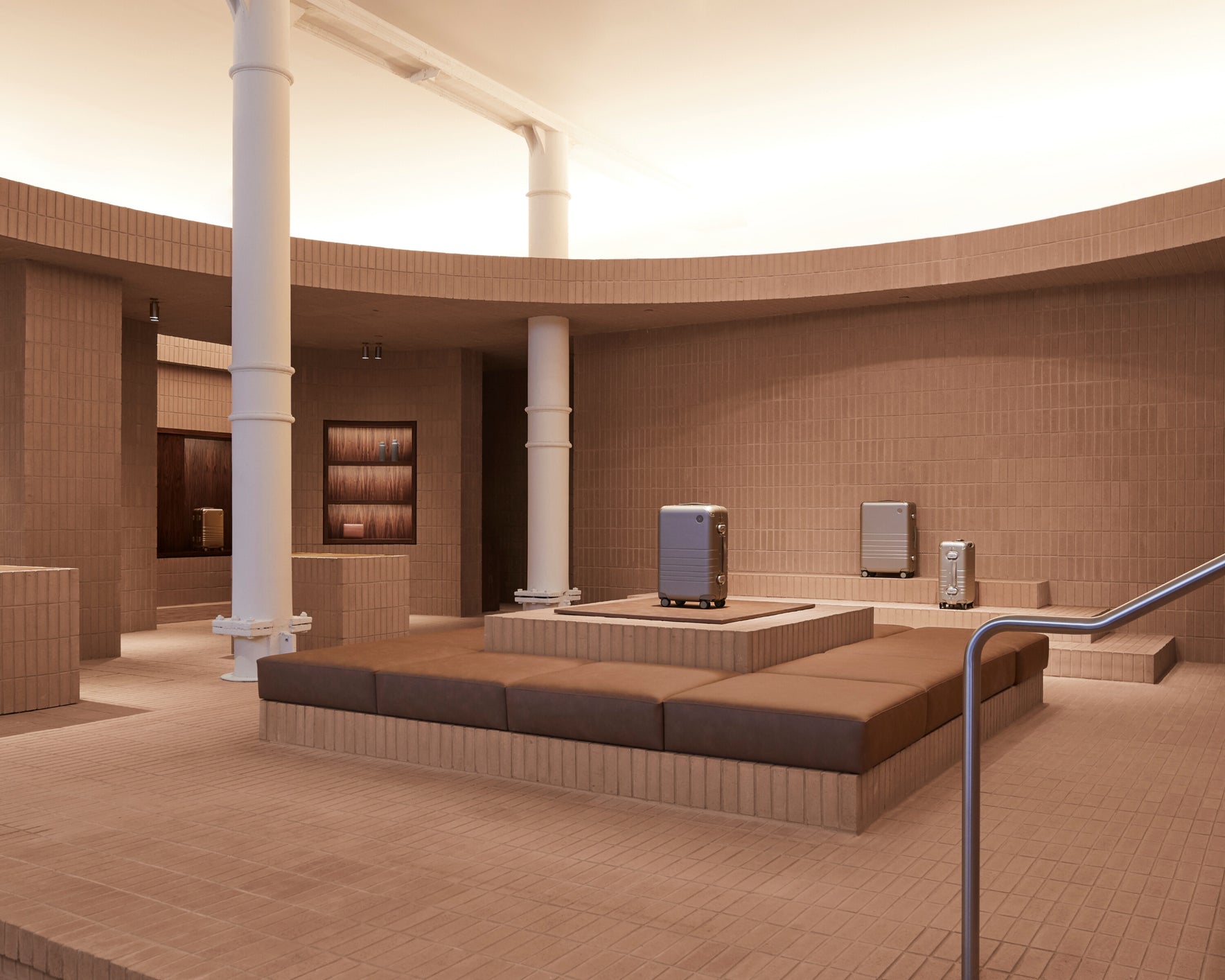 Monos SoHo store interior with terracotta brick textures, curved seating, and aluminum luggage displays.