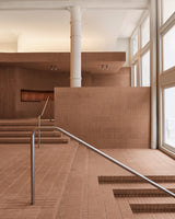 Sunlit entrance area of the Monos SoHo store featuring terracotta brick steps, white columns, and clean steel railings, with natural light streaming through large front windows.