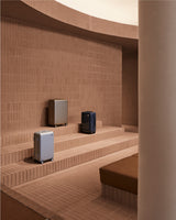 Aluminum luggage displayed on terracotta brick steps inside the Monos SoHo store, framed by warm light and curved architectural lines.