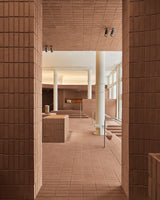 Architectural view through the Monos SoHo store, showing terracotta brick walls, white columns, and minimalist displays softly illuminated by natural light from large front windows.