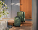 Monos Expandable Carry-On and Expandable Check-In Medium in Olive Green on wooden steps.