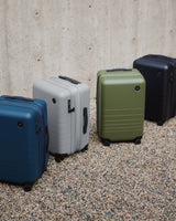 Lineup of Monos Expandable Carry-On suitcases in Blue, Silver, Olive, and Black.