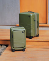 Monos Expandable Carry-On and Expandable Check-In Medium in Olive Green on wooden steps.